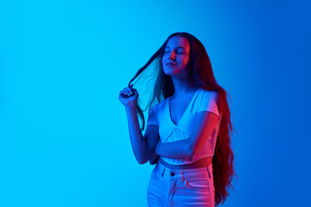 Fantasies. Young woman standing with closed eyes and dreaming face against blue studio background in neon lightの写真素材