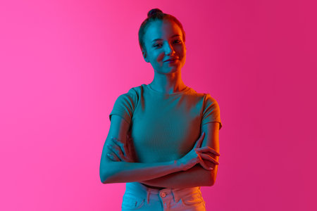 Beautiful young girl with hairbun, smiling, looking tenderly at camera against pink studio...