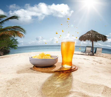 Glasses of delicious lager beer with with chips appetizers on sand against ocean, palms and blue sky backgroundの写真素材