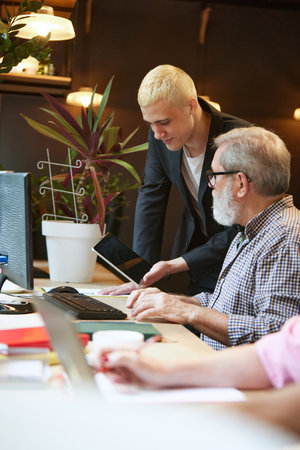 Young and senior man working together in modern office, talking about projects and strategies. Cooperationの写真素材