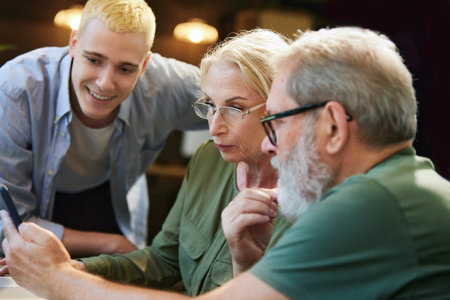 Concentrated business people, young man and senior colleagues working together in office, looking on mobile phoneの写真素材