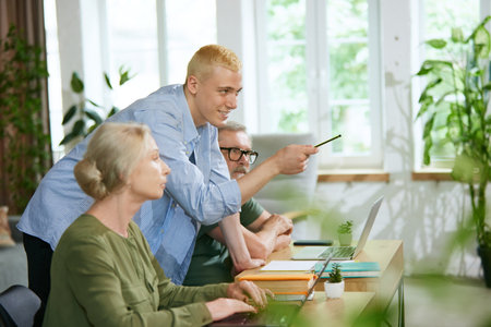Young man explaining senior people how to use laptop apps for business purposes. Assistance and cooperationの写真素材