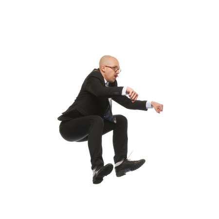 Bald man in suit and glasses jumping in position of driving bike isolated on white backgroundの写真素材