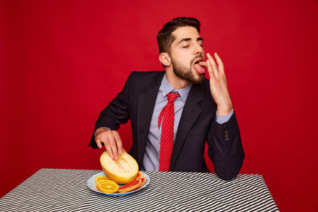 Portrait of seductive man in official suit touching mean against red background. Passion and hidden tasteの写真素材