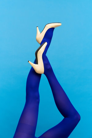 Slender womans legs wearing stylish, heeled white shoes and blue tights over blue backgroundの写真素材