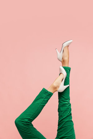 Female legs in white heeled shoes and green pants over pink background. Smart casual, business styleの写真素材