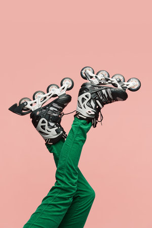 Female legs wearing rollers and green pants over pink background. Active lifestyle and sport