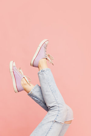 Casual, comfortable look. Female legs wearing jeans and sneakers over pink backgroundの写真素材