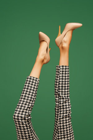 Female legs in heeled beige shoes and in checkered pants over green background. Smart casual, business styleの写真素材