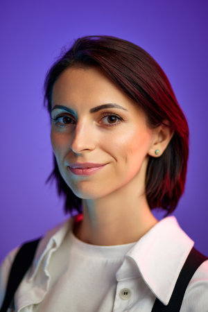 Portrait of beautiful woman in her 30s with short hair, looking at camera against purple studio...