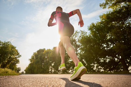 Back view dynamic image of sportsman, runner in sportswear training, running alone the road