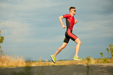 Speed and endurance. Motivated sportsman in sportswear running along the road, training outdoors. Side viewの写真素材