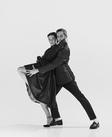 Rhythm and freedom. Black and white. Beautiful young woman in elegant black dress dancing with stylish and handsome manの写真素材
