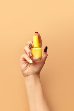 Female hand holding nail polish against beige background. Multicolored pastel manicure. Posterの写真素材