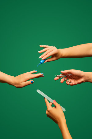 Female hand painting nails with blue polish, holding scissors and nail file against green background. Salon careの写真素材