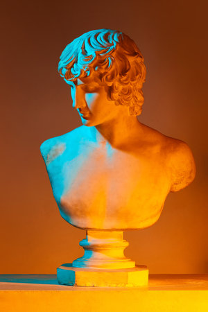 Antique statue bust against yellow studio background in neon lights. Plaster copy of greek sculpture. Concept of art and mythologyの写真素材