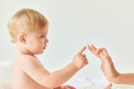 Tender touch. Little baby girl, child sitting in bed, toughing mothers finger with cream. Beauty products for babiesの写真素材