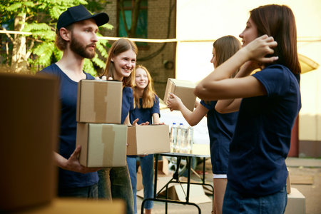 Young people, man and women, volunteers packing boxes into van outdoors. Picking help for people in needの写真素材