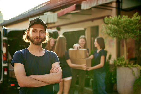 Focus on young man, volunteer standing outdoors near van on sunny day. Young people on background...