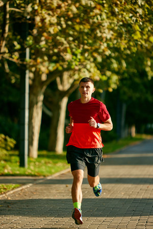 Dynamic image of young muscular man, athlete in motion running in early morning in park, training...
