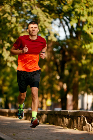 Sunny morning outdoor training. Muscular, athletic man in sportswear, runner in motion, running in...