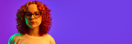 Portrait of teen girl with curly redhead hair, looking a camera against purple background in neon lightの写真素材