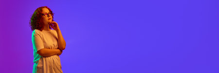 Teen girl with curly hair standing with thoughtful face and looking away against purple background...