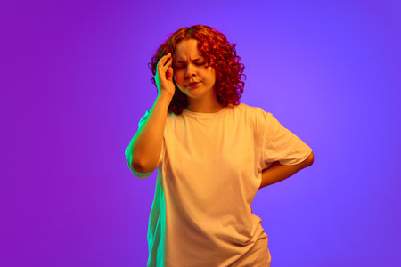 Teen girl holding hand on head, having headache, feeling irritation against purple background in...