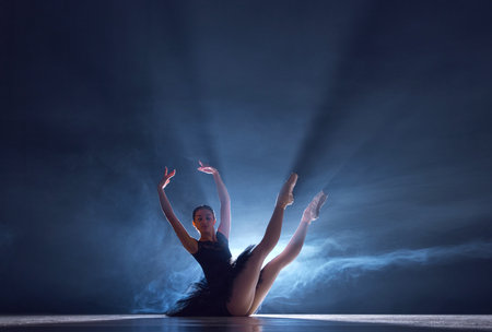 Elegance and grace in movements. Beautiful ballerina dancing over blue background with spotlightの写真素材