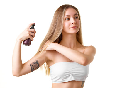 Pretty young girl taking care after blonde hair, sing spray and heat protection isolated over white studio backgroundの写真素材