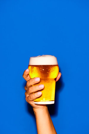 Female hand with glass with lager, foamy, cool beer isolated on blue background. Posterの素材 [FY310216033719]