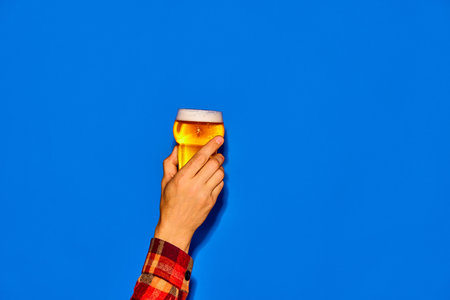 Male hand holding glass with chill, lager, foamy beer isolated on blue background. Delicious taste. Posterの写真素材