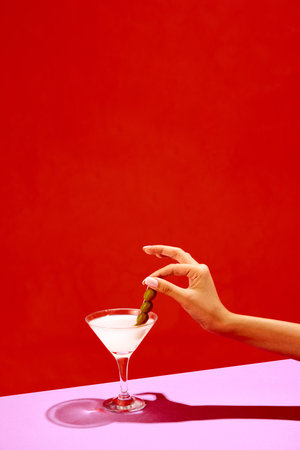 Traditional original drink. Glass with martini decorated with olives isolated over red background. Salty taste of appetizer. Posterの写真素材
