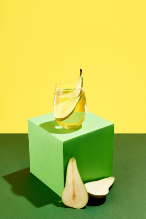 Delicious, sweet cocktail with pear taste standing on green cube over yellow background. Summer...