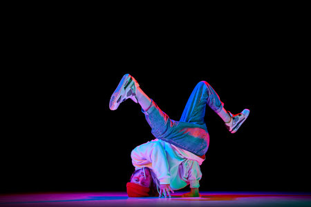 Dynamic image of man in his 30s in motion, dancing breakdance isolated over black studio background...