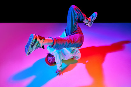 Dynamic image of man in his 30s in motion, dancing breakdance isolated over black studio background in neon lightの写真素材