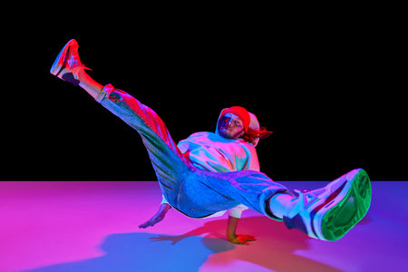 Young man in sportswear in motion, dancing breakdance isolated over black studio background in neon...