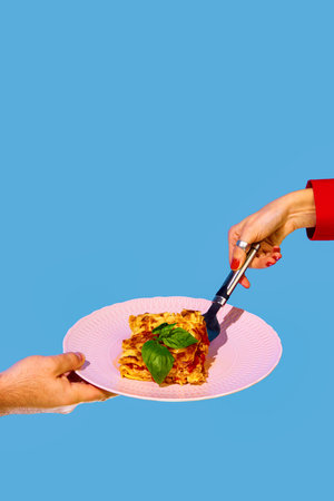Female hand serving delicious Italian food, putting lasagna on plate over green and blue backgroundの写真素材