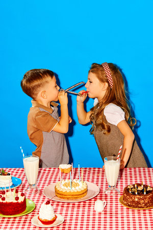 Playful, happy little boy and girl, children paying with birthdays toys, celebrating against blue studio backgroundの写真素材