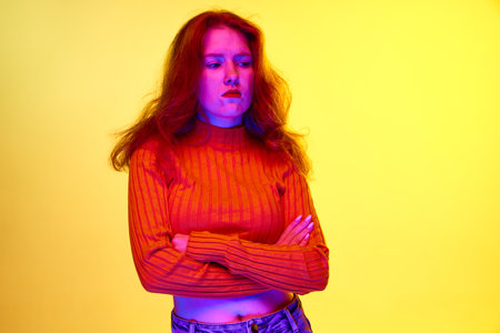 Offended face. Young girl standing with unhappy, unpleasant face against yellow studio background in...