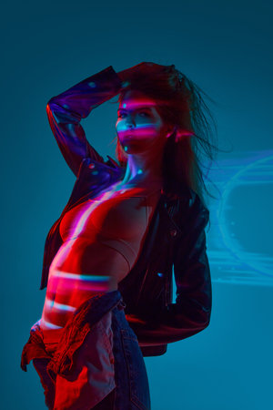 Beautiful, sensual young girl in underwear posing against blue background with neon lights reflection on body and faceの写真素材