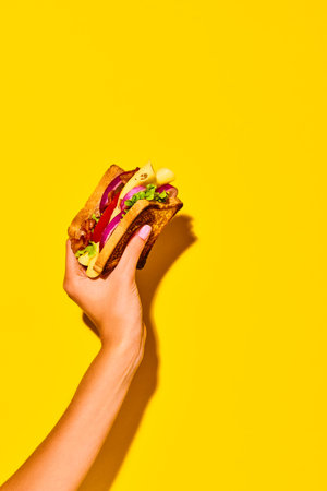Woman holding delicious sandwich with grilled bread, ham, lettuce, cheese, tomato, onion and avocado over yellow background. Cooking, taste. Posterの写真素材