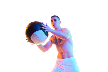 Athletic young man with strong, muscular body training with fitness ball against white studio background in neon lightの写真素材
