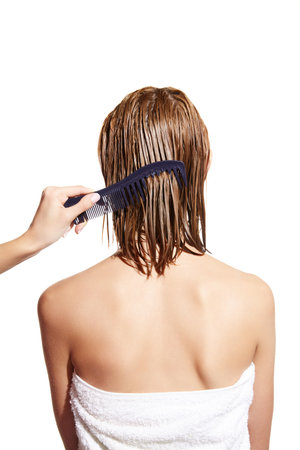 Female hand brushing wet blonde hair of a girl against white studio background. Taking care after hair lookの写真素材