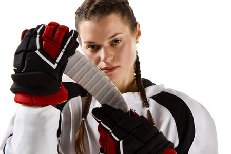 Portrait of young beautiful girl, hockey player in uniform standing with stick isolated over white...