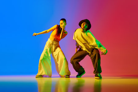 Expressive, talented, artistic young man and woman, hip hop dancers in motion, performing against blue red background in neon lightの写真素材