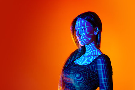 Portrait of beautiful young woman posing against orange studio background with neon reflection. Fluorescent artの写真素材