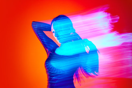 Portrait of young woman posing against orange studio background with neon reflection, mixed lights. Fluorescent lightの写真素材
