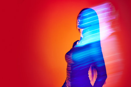 Portrait of young woman posing against orange studio background with neon reflection, mixed lights. Fluorescent lightの写真素材