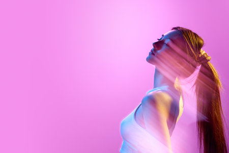 Portrait of beautiful young woman, elegant girl posing against light purple background in neon lights. Neon lights smashesの写真素材